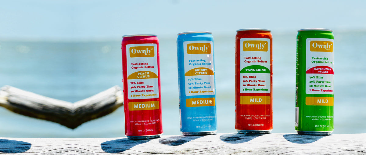 Four Ownly seltzers lined up by the water